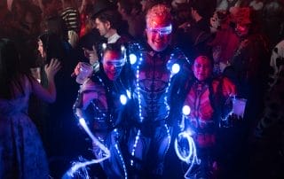 Three attendees in glowing, futuristic costumes pose together at a lively Halloween party in Denver.
