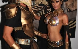 Couple in elaborate Egyptian-themed costumes posing together against a decorative backdrop at the event.
