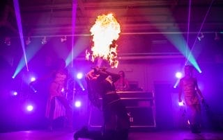 Fire performer creating a dramatic display on stage with dancers in the background at the Halloween event in Denver.