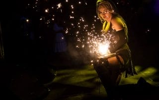 Performer creating sparks on stage at Paranormal Palace, surrounded by a smoky atmosphere and dim lighting.