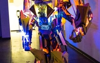 A large, illuminated robot resembling a transformer stands in a dimly lit hallway at the Halloween event.