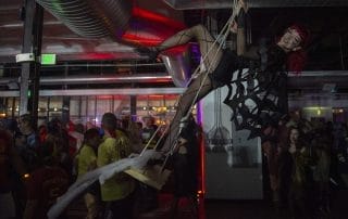 A performer in a spider web costume swings above a lively crowd at the Halloween event in Denver.