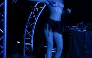 Performer in a sparkling costume dancing on stage under blue lights at the Paranormal Palace event in Denver.