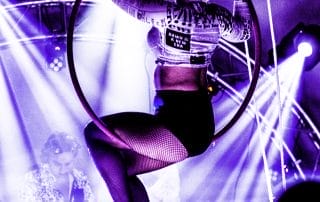 Aerial performer in a hoop surrounded by purple lights at a Halloween event in Denver.