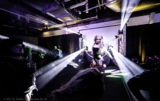 Performer in a striking outfit dancing on stage with dramatic lighting at the Halloween event in Denver.