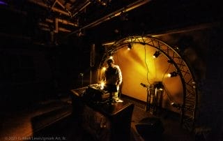 DJ performing at a lit stage with an arch backdrop during the Paranormal Palace event in Denver.