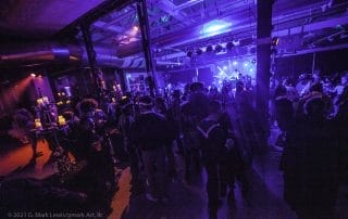 Crowd dancing under purple lights at a Halloween party, with candles illuminating the space in the background.