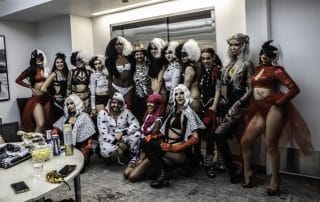 A group of costumed performers posing together, showcasing a variety of Halloween-themed outfits and accessories.