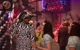 A performer in a zebra-patterned bodysuit and hat interacts with two women in vintage dresses at the Halloween event.