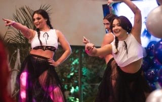 Three dancers in matching outfits perform on stage, smiling and engaging with the audience at Paranormal Palace.